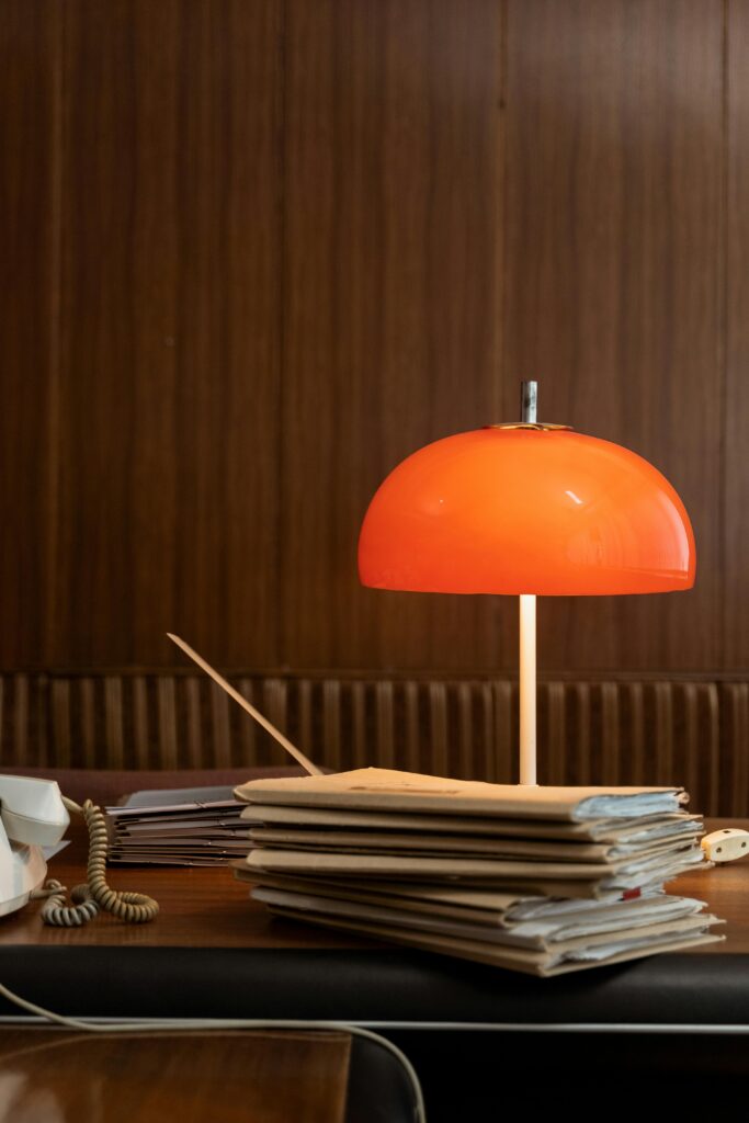 pexels photo 8872548 8872548 Retro office setting with a red lamp and stacked folders on a wooden desk, capturing a vintage vibe.